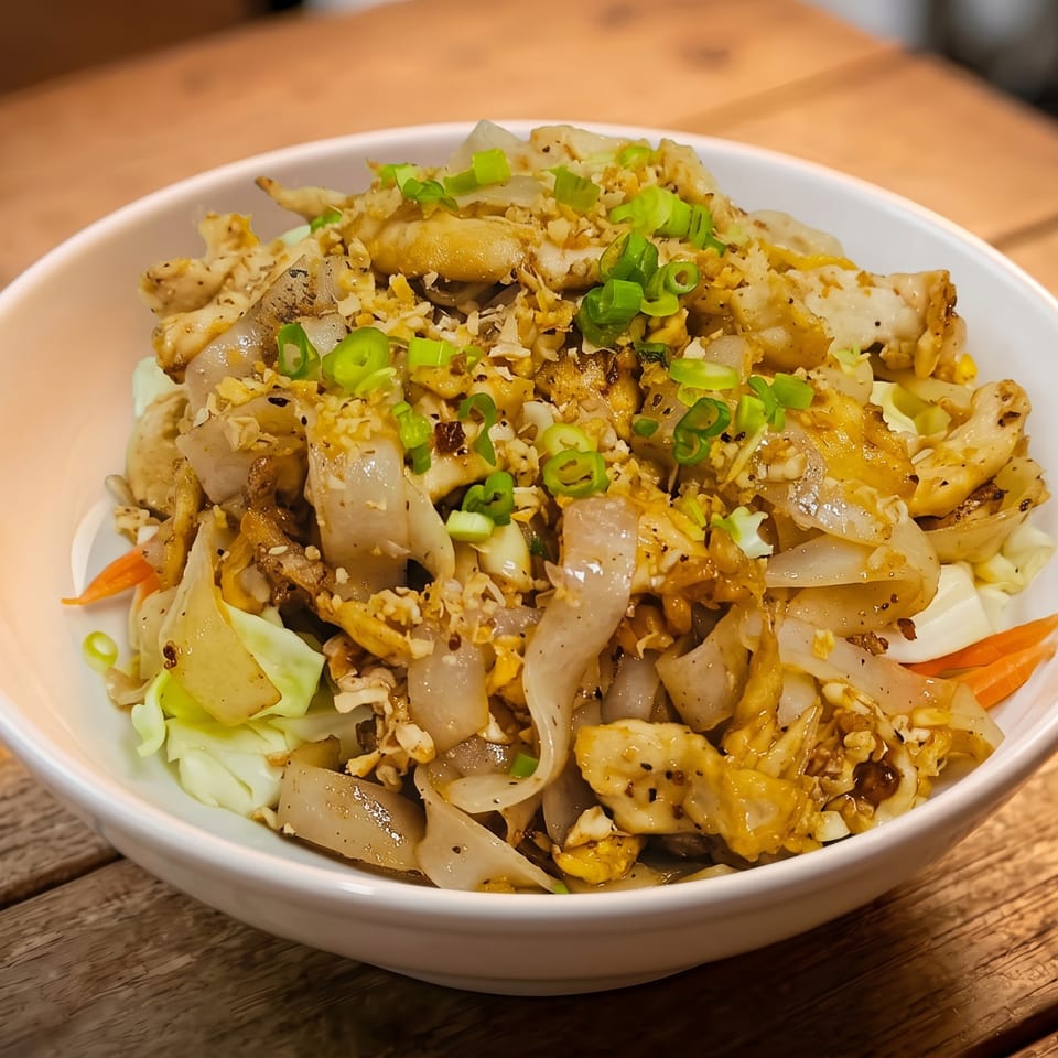 A white bowl filled with stir-fried noodles, chicken, vegetables, and garnished with green onions.